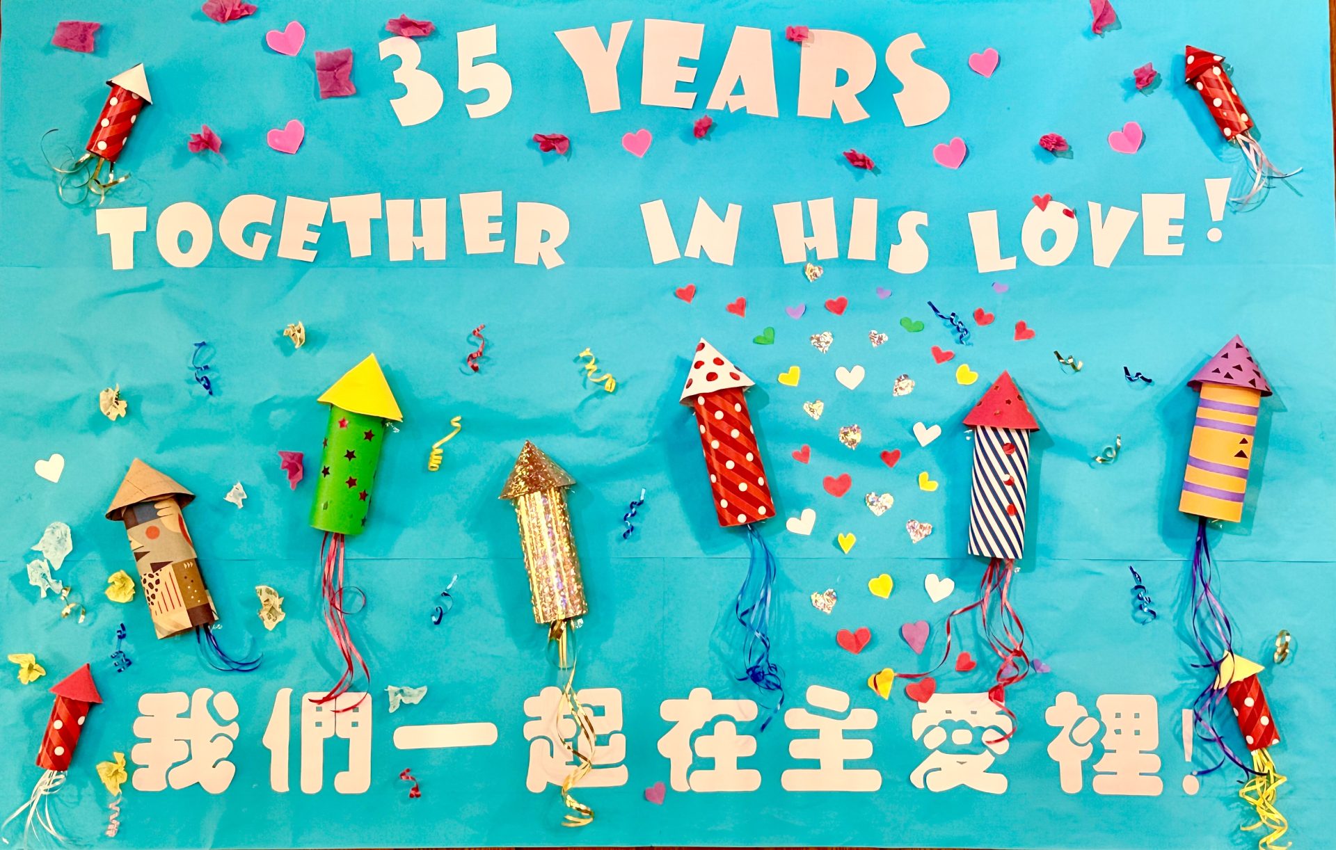 Handmade 35th anniversary banner reading "35 Years Together in His Love / 我們一起在主愛裡", decorated with paper fireworks and hearts